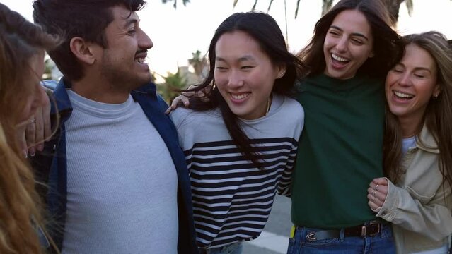 Diverse group of young adult friends having fun hugging each other outside. Joyful millennial people laughing enjoying time together. Community and friendship concept