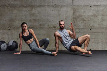 An attractive couple in the gym engaging in various stretching exercises together, showcasing their...