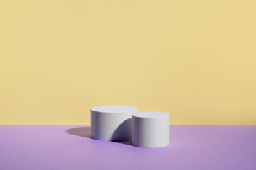 Two empty white round podiums on purple and yellow background. Showcase for product presentation. Pedestal for beauty cosmetic advertising. Minimal still life. Copy space, front view.