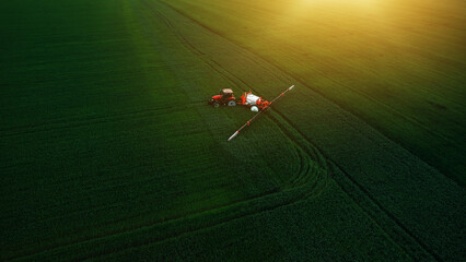 Aerial  view of tractor spraying pesticides on wheat  field with sprayer  in spring.
