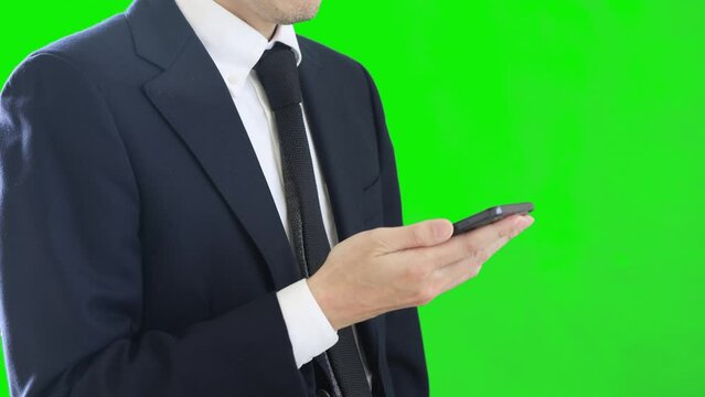 片手でスマートフォンを操作するビジネスパーソン。スーツを着ている男性。グリーンバック。