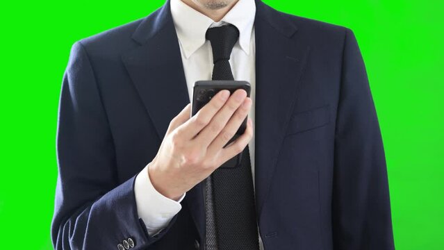 スマートフォンを操作するビジネスパーソン。スーツを着ている男性。グリーンバック。