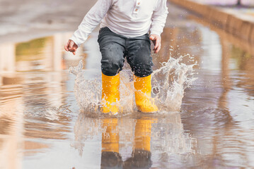 Child's feet in yellow rubber boots jumping over a puddle in the rain