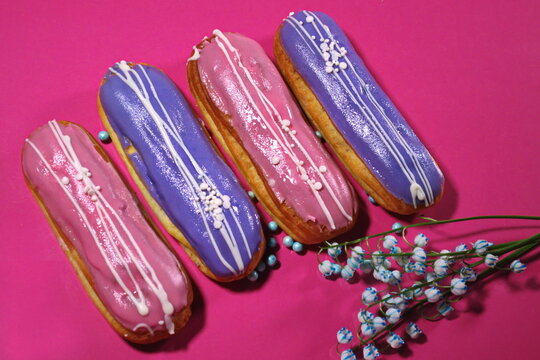 french dessert Eclair cake with pink  violet creme shining decoration Filling glaze with strawberries  blueberries Pink background Effect of levitation lily of the valley flowers painted blue elegant