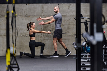 Fototapeta na wymiar A muscular man assisting a fit woman in a modern gym as they engage in various body exercises and muscle stretches, showcasing their dedication to fitness and benefiting from teamwork and support