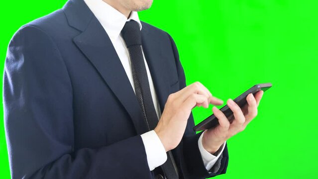 両手でスマートフォンを操作するビジネスパーソン。スーツを着ている男性。グリーンバック。