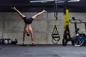 A muscular man in a handstand position, showcasing his exceptional balance and body control while performing a variety of exercises to enhance his overall body stability and strength in a modern gym