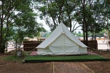 Exterior of white teepee tent at glamping place surrounded by green trees.