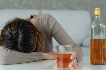 Depressed young Asian woman addicted feeling bad drinking whiskey alone at home, stressed...