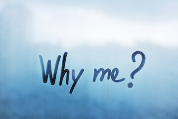 Written finger words why me on blue foggy glass on wet window