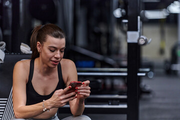 A fit woman in the gym taking a break from her training and uses her smartphone, embracing the convenience of technology to stay connected