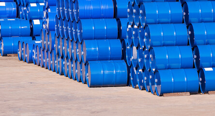 Piles of many blue oil drums stacked on industrial yard area in perspective side view