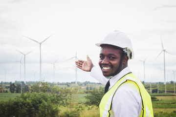 African male engineers working on site with wind turbine propeller on the background. Alternative...