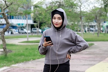 Asian young muslim women using phone after doing stretching exercise at city park