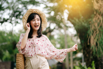 Portrait of asian young woman traveler with weaving hat and basket happy smile on green public park...
