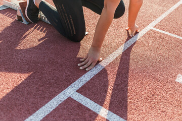 Caucasian woman at the athletic track starting point, hands on the start line and legs on starting...