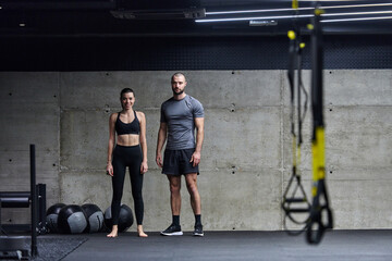 Naklejka na ściany i meble Muscular man and fit woman in a conversation before commencing their training session in a modern gym.