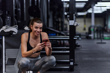 A fit woman in the gym taking a break from her training and uses her smartphone, embracing the convenience of technology to stay connected