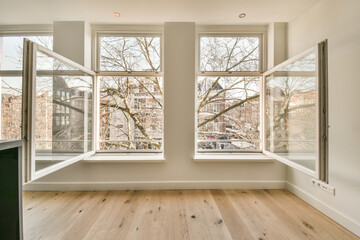 two windows in a room with wood flooring and bare tree branches on the window sies, looking out onto an urban street