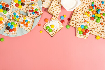 Pieces of matzah covered with cream cheese and colorful candies for Jewish holiday Pesach on pink...