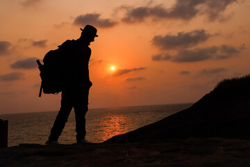 the silhouette image of a young boy who is traveler standing in front of sunset