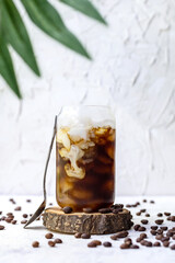 Glass of ice coffee with cream being poured into it showing the texture of drink on white