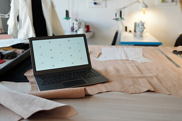 Workplace of tanner or taillor with laptop standing on beige suede or leather textile with paper...