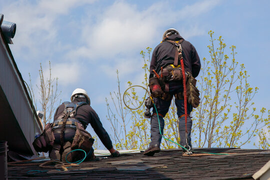 two mans fixing asphalt shingles working on a roof with security rope