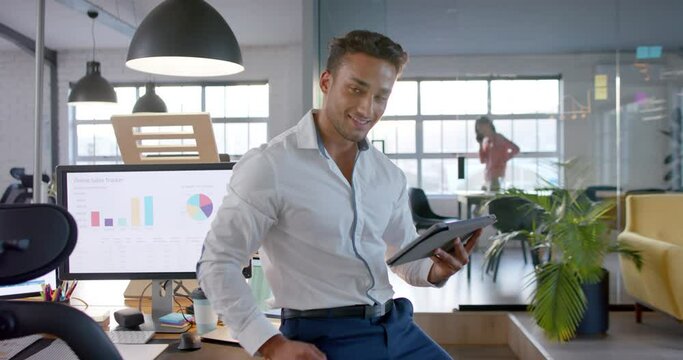 Portrait of happy smart casual biracial businessman using tablet in office, smiling, in slow motion