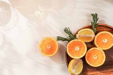 Oranges lemons rosemary, citrus fruits on a wooden plate shadow of a palm leaf. Summer citrus background.