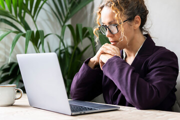 Professional entrepreneur reading email on laptop at the desk wearing glasses with concentration. Portrait of confident businesswoman. Freelance female activity online. Modern job business lifestyle - obrazy, fototapety, plakaty
