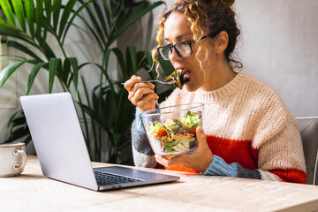 Woman busy working on laptop and eating a salads at the same time. Fast lunch break for online job...