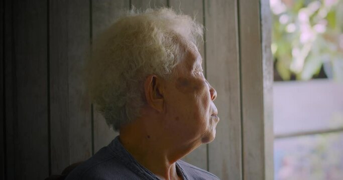 Close-up shot : An Asian farmer woman who was a poor rural elderly person with white hair sitting lonely at her doorstep.