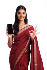 Cheerful Indian young traditional woman holding smartphone showing ok hand gesture. 
