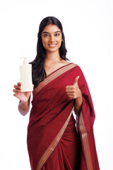 Young Indian woman holding a cream bottle cheerful and confident showing thumbs up.