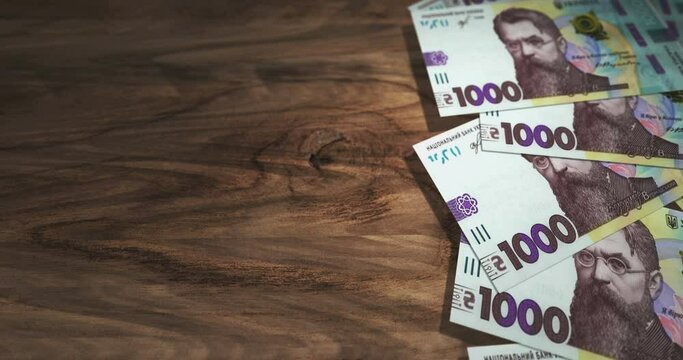 Ukrainian Hryvnia 1000 UAH banknotes on the wooden table. Ukraine currency paper notes 3D concept background. Seamless and looped.