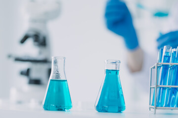 medical or scientific researcher researching and experimenting Multi-colored solution, vial and microscope In the laboratory or in the laboratory by wearing blue gloves and white clothing completely.