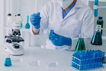 medical or scientific researcher researching and experimenting Multi-colored solution, vial and microscope In the laboratory or in the laboratory by wearing blue gloves and white clothing completely.