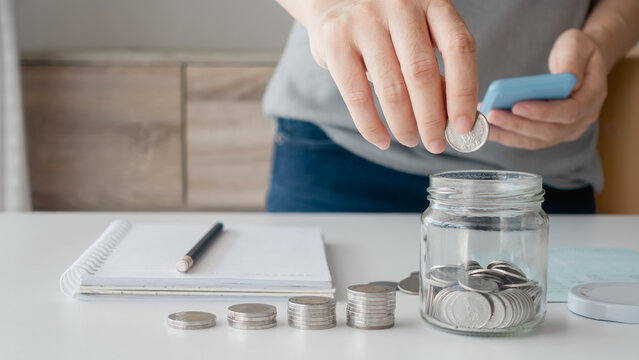 Close-up image of businesswoman hand holding coins putting in piggy bank glass with a calculator to calculate concept saving money for business investment-finance accounting.