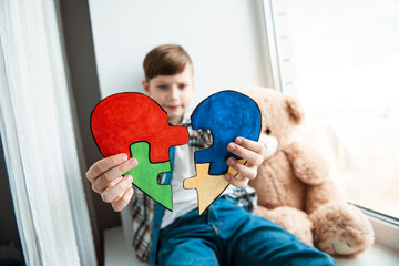 A cute boy holds a puzzle in the form of a heart. World autism awareness day, Mental health care,...