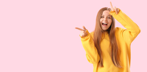 Laughing young woman showing loser gesture on pink background with space for text