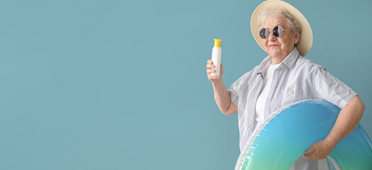 Senior woman with sunscreen cream and inflatable ring on color background with space for text