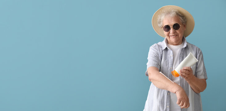 Senior woman applying sunscreen cream on her skin against color background with space for text