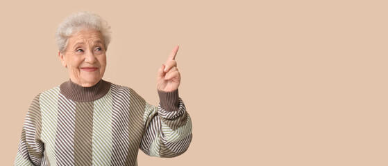 Senior woman pointing at something on beige background with space for text