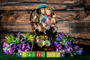 Fototapeta na wymiar life is good spelled with wood blocks with flowers and child dolls