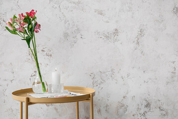 Burning candle and vase with alstroemeria flowers on table near grey grunge wall