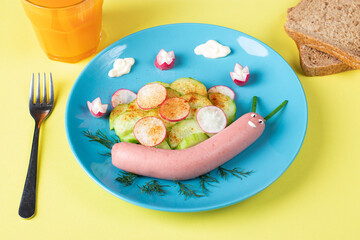 Funny snail from sausage with cucumber and radishes salad on a plate - food idea for kids, High angle