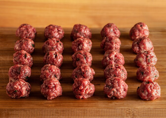 Raw uncooked meatballs on wooden cutting board.