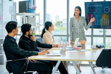 Pretty Asian business woman stand to present the project using TV or monitor in front of other co-workers and manager also discusss to get success in office with day light.