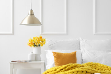 Vase with beautiful narcissus flowers on bedside table in interior of bedroom